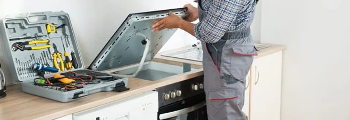 Cooktop repair technician lifting a built-in stovetop for service in Mesa, AZ